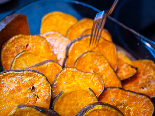 Roasted sweet potato slices in a glass baking dish with a fork. Close-up of baked sweet potatoes...