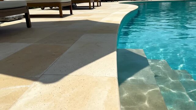 Video of sunlit pool deck with drifting umbrella shadow, outdoor relaxation theme, hospitality and travel concept with clean summer aesthetic.