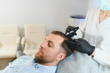 Fototapeta premium Side view of handsome man getting hair treatment at beauty salon. Man having mesotherapy session at aesthetic clinic, therapist hands in gloves making injection in scalp