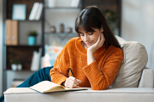 Calm freelance writer focused on writing in a notebook on a cozy couch