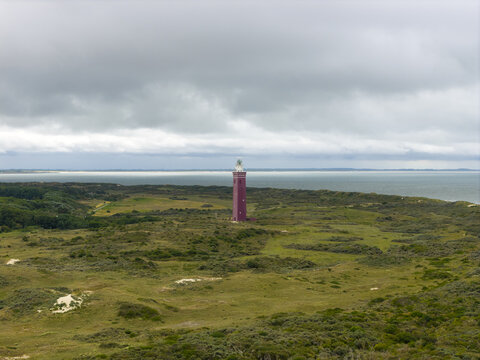 Aerial view of a striking red lighthouse piercing the horizon, standing tall amidst the green and brown fields, under a cloudy sky, Ouddorp, Zuid-Holland, Netherlands.