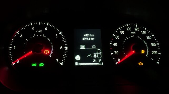 Wide view of illuminated car dashboard at night showing tachometer needles, parking brake warning light, digital mileage display, modern vehicle instrument panel, automotive technology concept