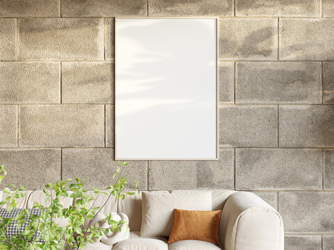 Vertical wooden poster frame mockup on a concrete block wall above a beige sofa with plant
