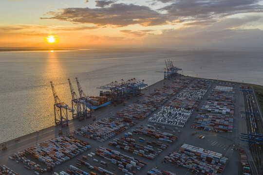 Aerial view of container ships and cargo containers, the port glows with the sunset's amber hues, casting long shadows across the industrial landscape, Bremerhaven, Bremen, Germany.