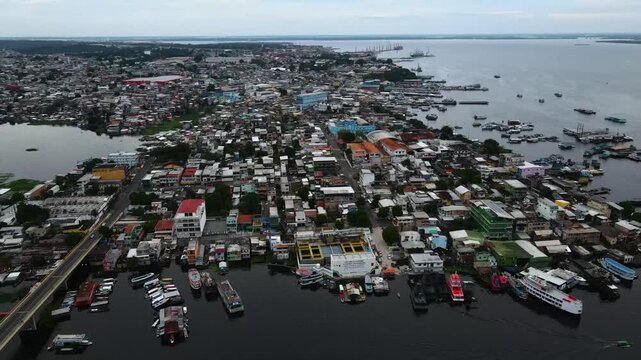 Black river and boat docking area in Manaus during a cloudy afternoon. Slow forward aerial looking at water, city and distant horizon. Recorded in 4K Apple ProRes 422.