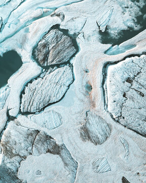 Aerial view of a frozen landscape where icy formations meet dark, still water, creating a stark contrast of textures and tones, Zermatt, Switzerland.