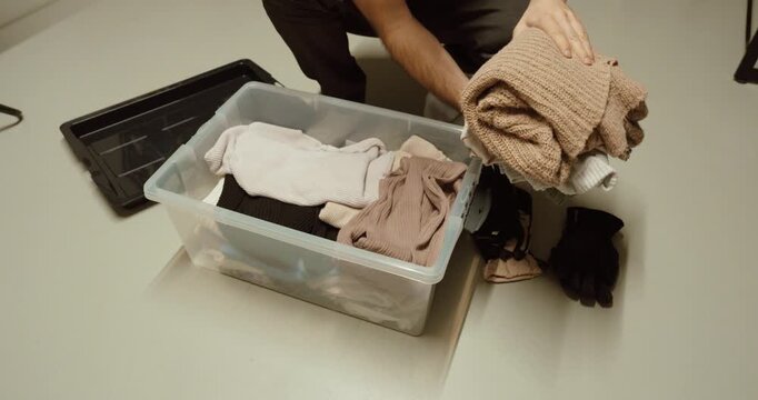 Person placing used clothes into a box for donation and recycling.