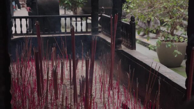 Static close-up shot of hundreds of red and brown incense sticks planted in ash inside a large stone censer with rising smoke at Luohan Temple courtyard in Chongqing, China