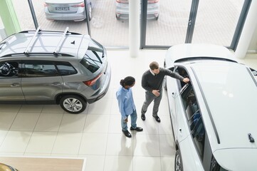 Car Sales Manager Showing Auto To Buyer Standing In Luxury Automobile Dealership Store