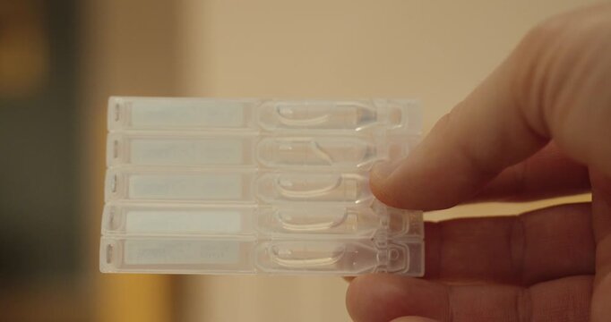 a hand holding single-use eye drop containers for eye care treatment.