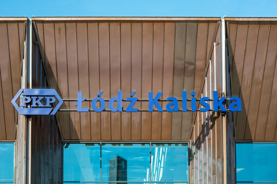 Blue PKP Ł&oacute;dź Kaliska signage on the modern copper facade of the railway station, architectural details of PKP station, public transport building branding in Ł&oacute;dź against metal wall panels.