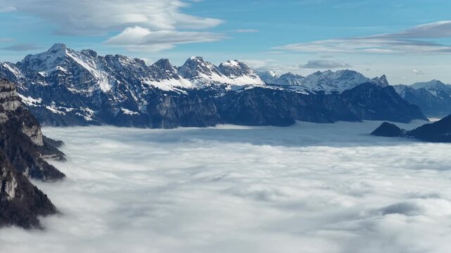 Snow covered alpine ridge rising above dense cloud inversion in Walensee valley under layered clouds, Switzerland