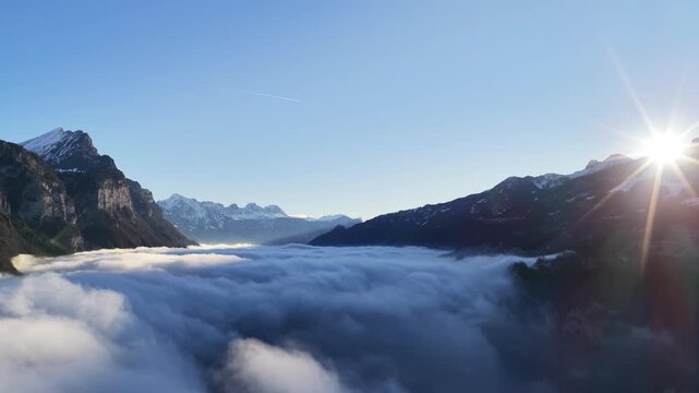 Bright sun rising above dense cloud inversion between mountain ridges in Walensee valley, Switzerland