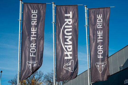 Triumph "For the Ride" promotional flags outside motorcycle dealership in Lodz, automotive branding and signage, modern visual identity, black flags against blue sky, outdoor marketing, motorcycle acc