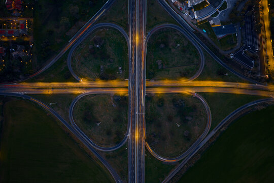 Aerial view of a cloverleaf interchange glows with golden light, cutting through the dark landscape, Rome, Lazio, Italy.