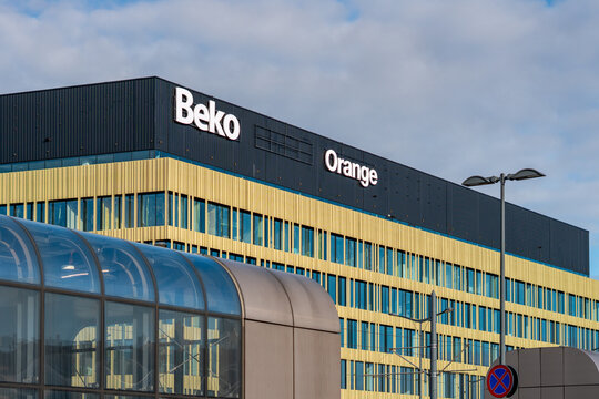 Modern office building featuring Beko and Orange logos, golden facade architecture, urban cityscape with corporate headquarters, public transport infrastructure, sunny day sky, professional commercial