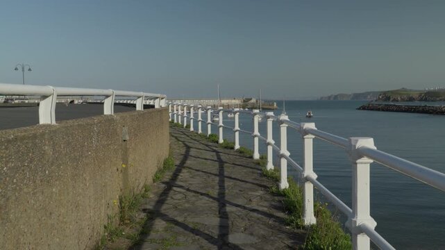 Coastal walkway with white railings following the harbor in Cand&aacute;s, Asturias, Spain. Scenic seaside path overlooking calm waters of the Cantabrian Sea with a peaceful maritime atmosphere.