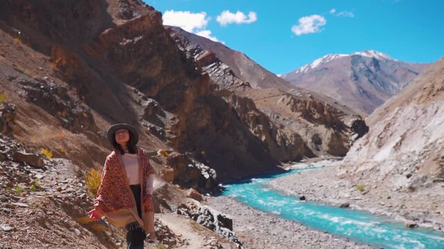 Indian teenager girl enjoying view of mountains and Tsarap river at Zanskar, Ladakh, India. Beautiful turquoise blue river flowing on the way to Phugtal Monastery. Travel, adventure, hiking and holida