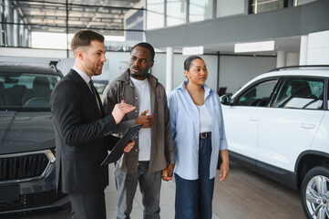 Car salesman showing vehicles to african american couple in dealership