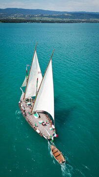 Yvoire, France - 27 July 2024: Aerial view of a stunning traditional sailing boat with white sails glides across the crystal-clear turquoise waters of Lake Geneva.