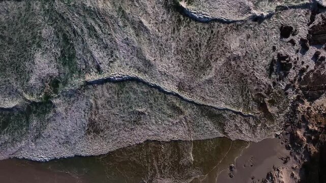 Aerial view of the ocean waves crashing onto the sandy beach, creating a mesmerizing pattern of white foam and dark water, Cape Town, Western Cape, South Africa.