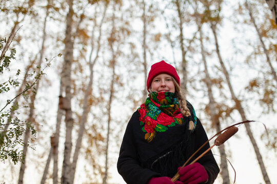 Smiling woman with red hat and scarf holding cattail in autumn forest