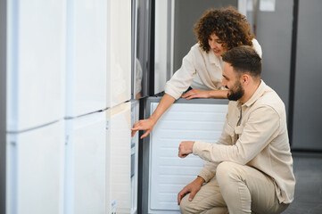 Couple choosing refrigerator in electronics store, woman pointing at appliance