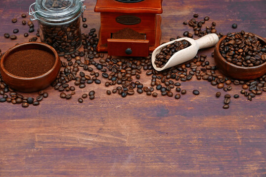 Kaffeebohnen, gemahlener Kaffee in Schalen, eine Kaffeem&uuml;hle mit offenem Fach und eine wei&szlig;e Schaufel auf einem Holztisch.
