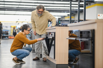 Fototapeta premium Mature couple choosing new built in oven in appliance store