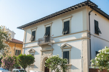 Fototapeta premium Traditional Italian residential house with green shutters under blue sky. Mediterranean architecture and sunny urban lifestyle concept