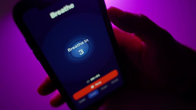 User using breathing exercise mobile app in dark room with purple backlight close-up