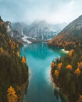 Aerial view of Lago di Braies with its turquoise waters reflecting the surrounding autumn colors and rugged mountains under a misty sky, Braies, Trentino-South Tyrol, Italy.