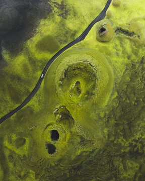 Aerial view of mossy hillocks puncturing the stark landscape, a lone car traversing the winding road, echoing Iceland's raw beauty, Skaftarhreppur, Iceland.
