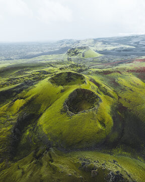 Aerial view of verdant volcanic craters punctuate the stark, moss-covered landscape, creating a surreal tapestry of textures and tones, Skaftarhreppur, Iceland.