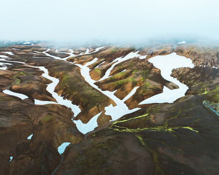 Aerial view of the stark, rugged landscape is softened by patches of snow and vibrant green moss clinging to the earth, Rangarthing ytra, Iceland.