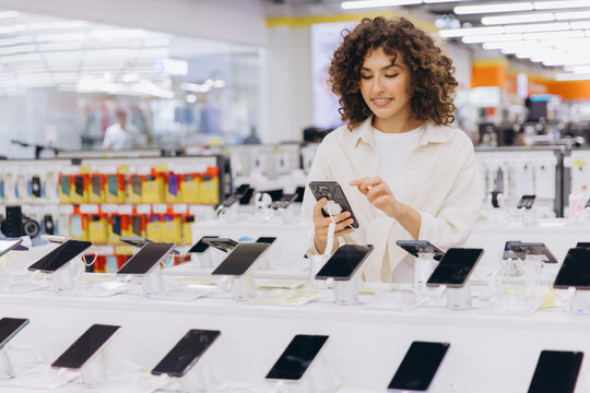 Woman shopping for a new smartphone, examining models on display in an electronics retail store