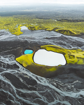 Aerial view of stark, black volcanic sands intertwine with vibrant green moss and glacial rivers, creating a surreal tapestry of color and texture, Skaftarhreppur, Skaftarhreppur, Iceland.