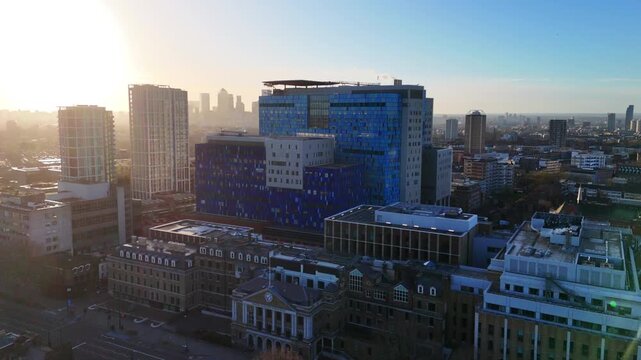 An aerial approach towards a modern hospital building with the sun rising over the city skyline.