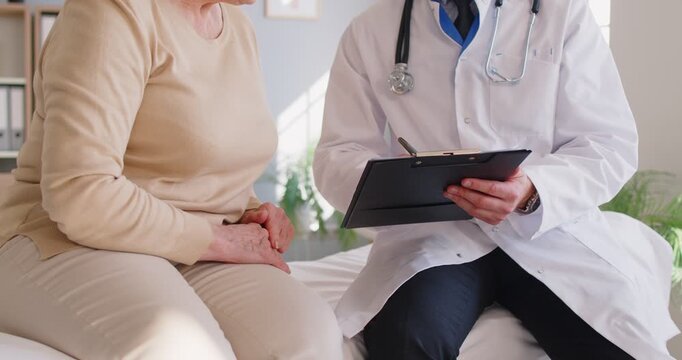 Elderly senior woman patient talking with male doctor or nurse sitting on couch in office discussing treatment or test results during medical examination in clinic. Medicine concept. 4k video.