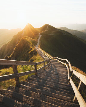 View of wooden steps descend into the valley as sunlight casts a golden glow over the mountains, creating a stunning vista, Mont-Dore, Auvergne-Rhone-Alpes, France.