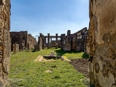 Lush peristyle in Pompeii Roman villa with central rainwater pool amid columns and grass, dramatic Mount Vesuvius looming behind ancient ruins.