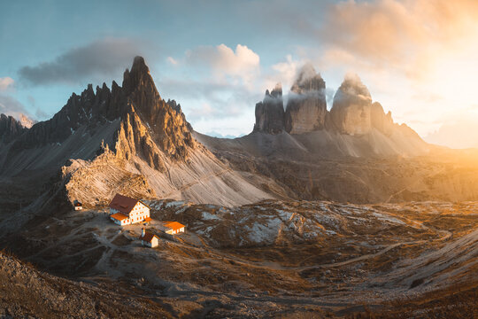View of jagged peaks rise majestically under a soft sky, casting long shadows across a landscape dotted with quaint buildings, Auronzo di Cadore, Veneto, Italy.