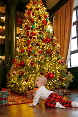 Baby crawls near a Christmas tree with lights and ornaments