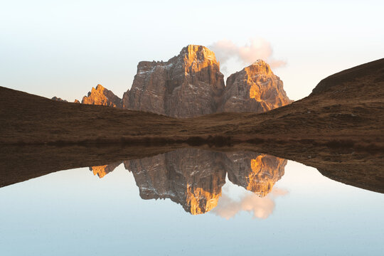 View of golden light kissing the rugged peaks mirrored in the tranquil lake, creating a serene, symmetrical tableau of nature's artistry, San Vito di Cadore, Veneto, Italy.
