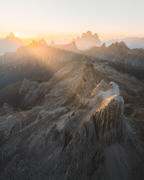 Aerial view of jagged peaks catching the golden rays of dawn, casting long shadows across the rugged terrain, San Vito di Cadore, Veneto, Italy.