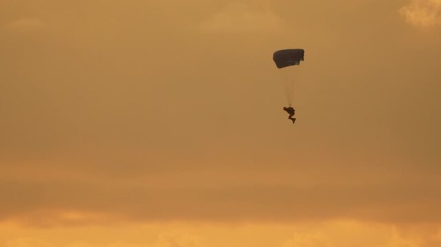 Skydiver parachute sunset glides through a golden sunset sky with a parachute capturing the freedom and adventure of extreme sports at dusk