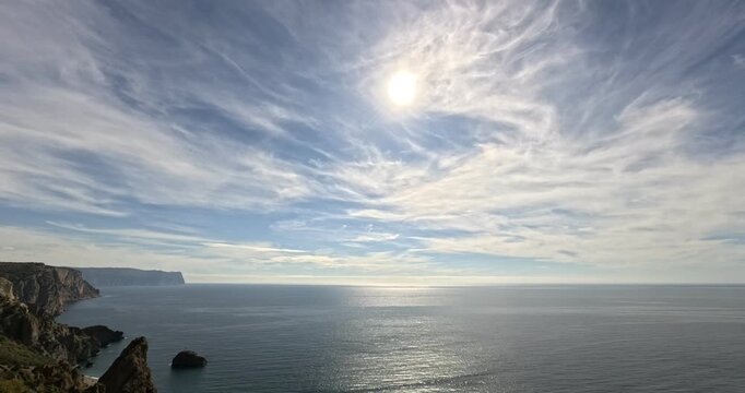 Seascape cliffs timelapse dramatic cirrus clouds move over peaceful blue ocean and sparkling water.