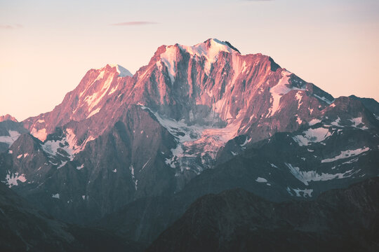 View of a majestic mountain peak kissed by the warm glow of the setting sun, its snow-dusted slopes contrasting with the deep blue shadows, Torbel, Wallis, Switzerland.