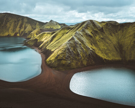 View of rugged, moss-covered mountains meet serene waters under a cloudy sky, creating a dramatic landscape, Skaftarhreppur, Iceland.