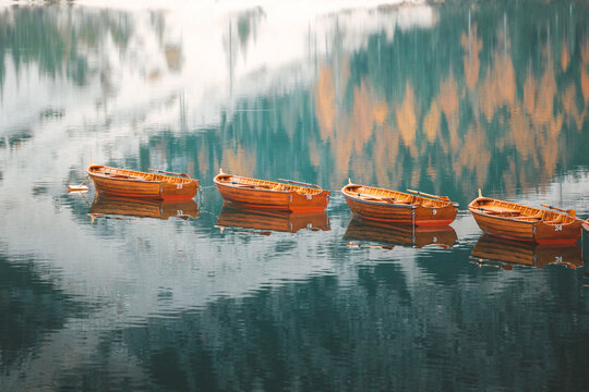 View of wooden boats adrift on the serene lake, reflecting the surrounding forest's autumn colors in a mirrored dance of nature, Bolzano, Trentino-South Tyrol, Italy.